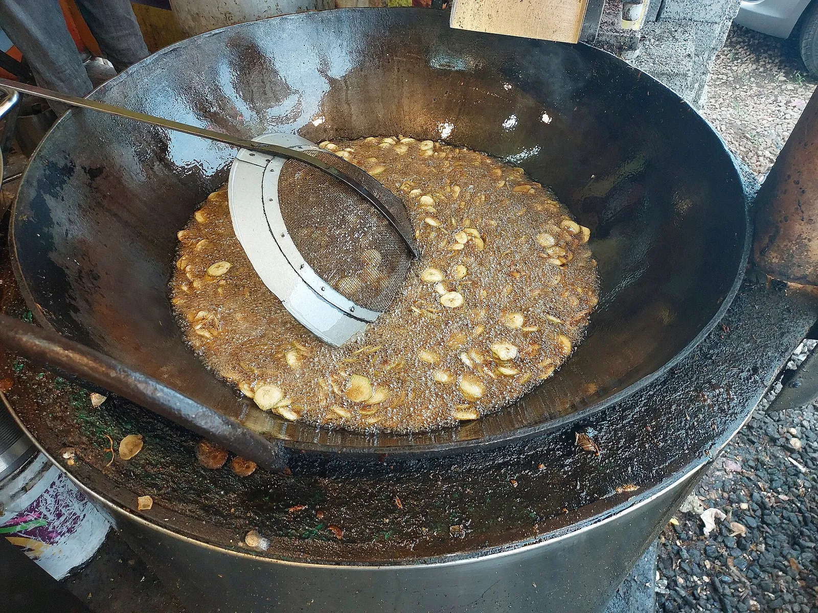 Raw Nendran banana being sliced into hot oil to make banana chips