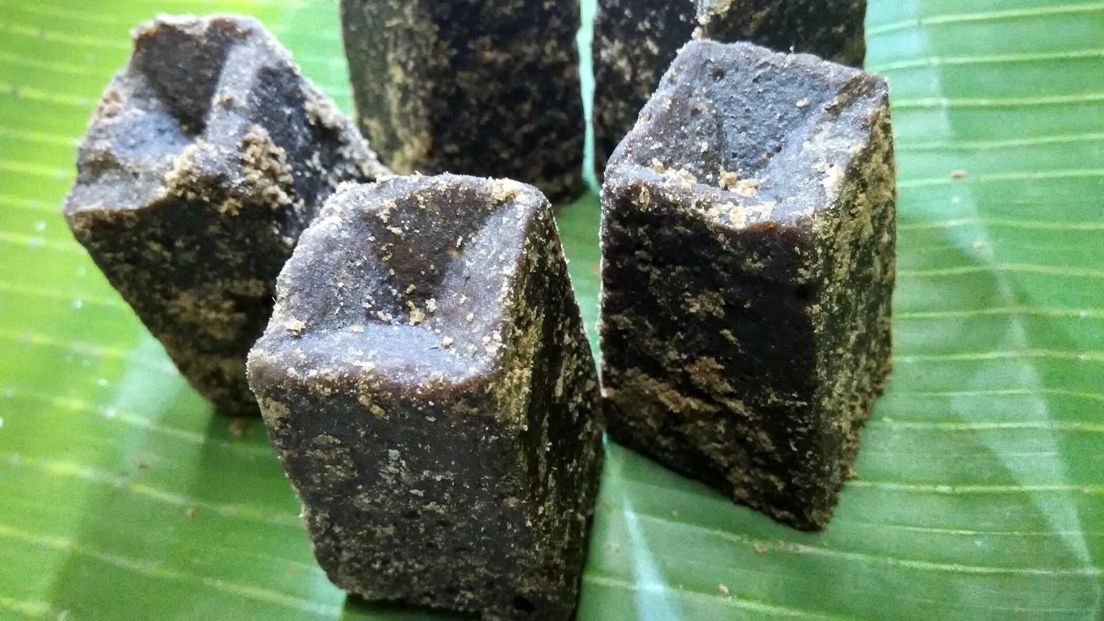 Blocks of dark Tamil Nadu palm jaggery (karupatti) set in moulds, resting on a banana leaf